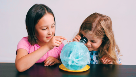 Two kids looking at a ball of ice with blue dye in it.