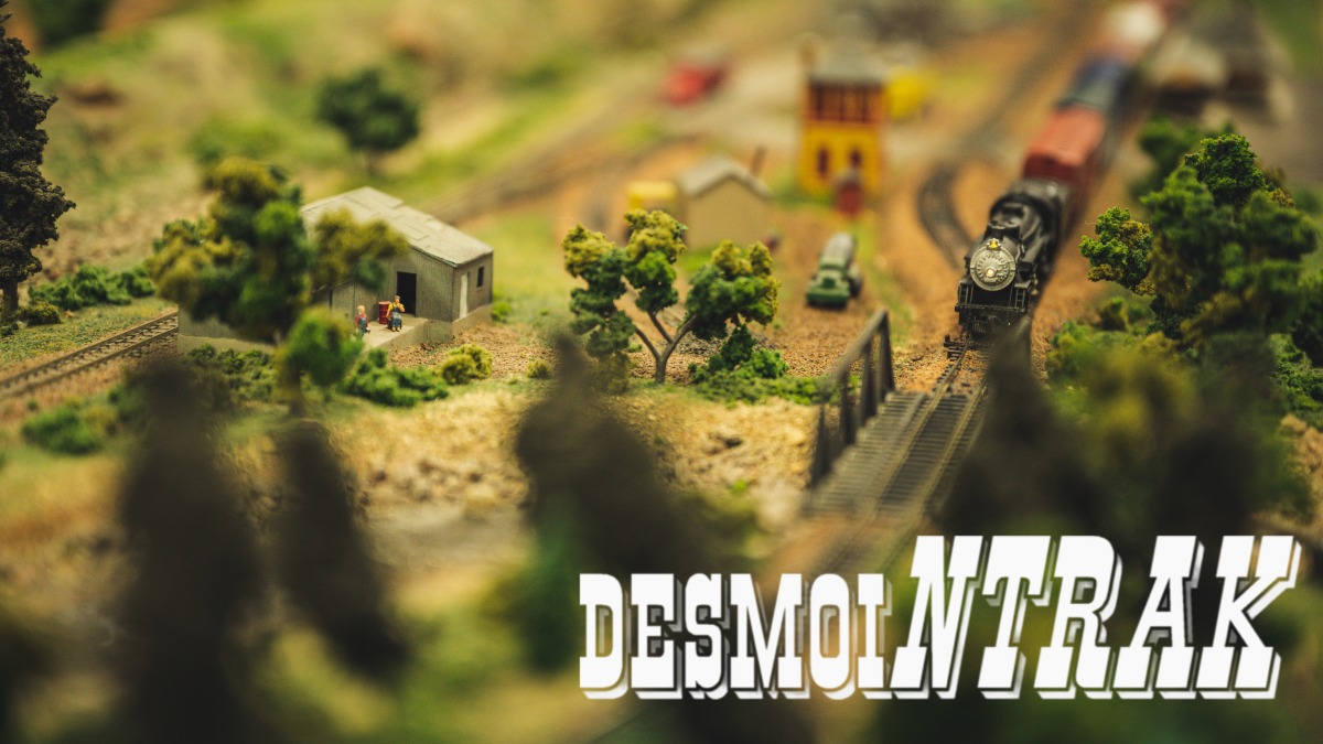 Image of a model train in a forest scene with the Des Moi NTrak logo in the bottom right corner.